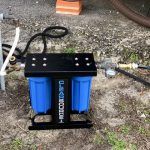 A blue water filter is sitting on the ground next to a hose.