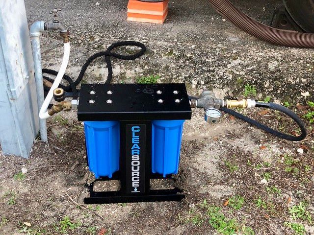 Blue and black RV water filter system on the ground, connected to water source.