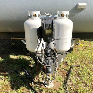 A trailer with two propane tanks attached to it is parked in the grass.