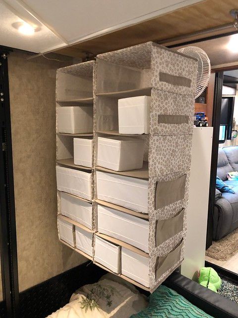 Hanging fabric organizer with cardboard shelves, mounted on a wall in an RV, with a fan visible.