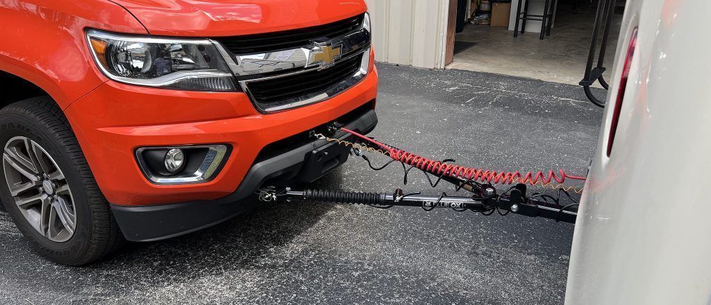 Red Chevrolet truck towing a white trailer. A coiled red cable connects them.