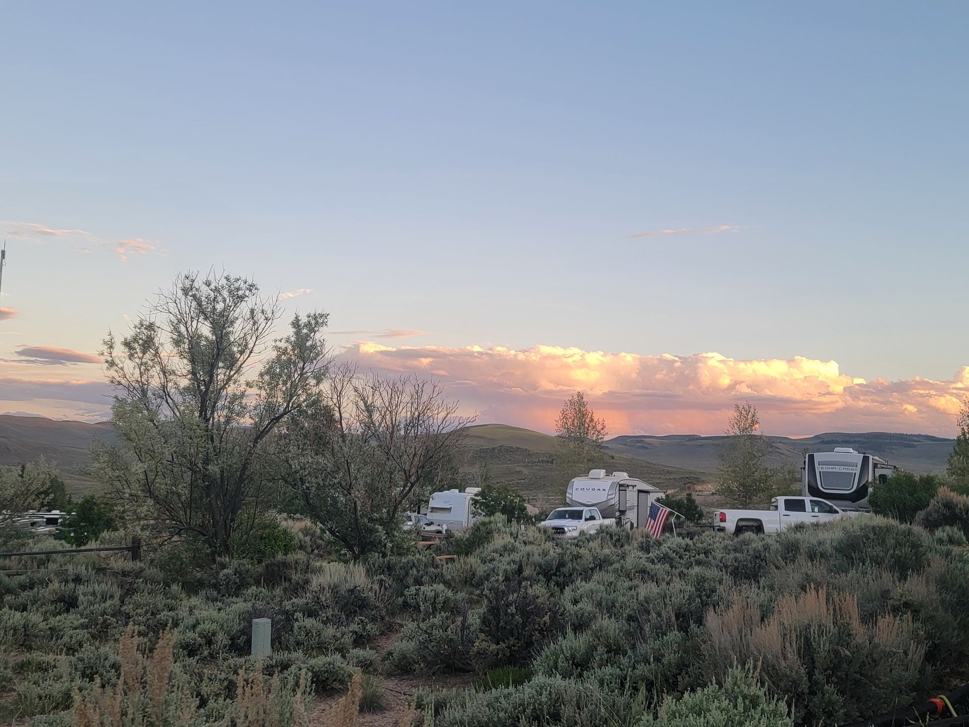 Campground with RVs and cars among desert foliage under a sunset sky with pink and orange hues.