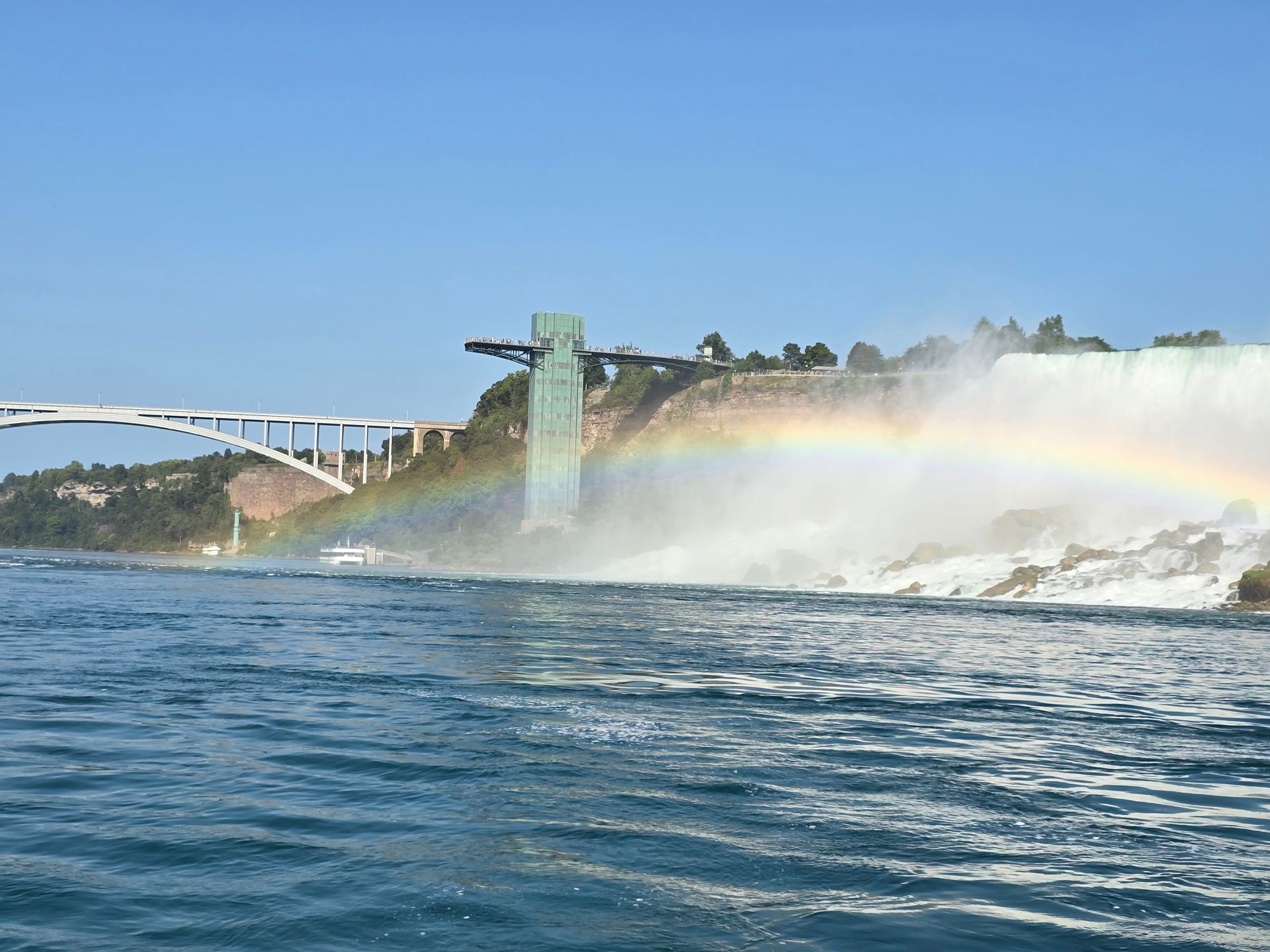 A waterfall with a bridge in the background and a rainbow in the water