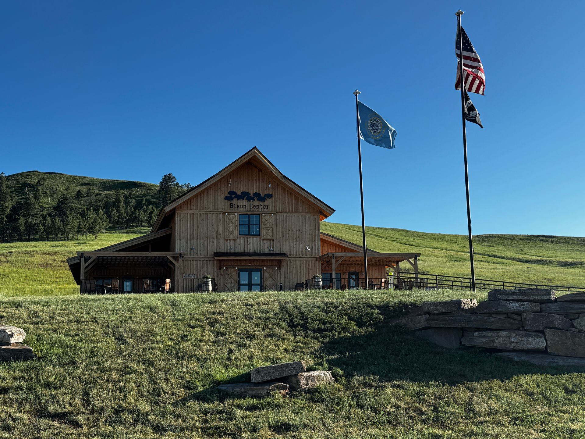 Wooden building with flags on a grassy hill under a blue sky.