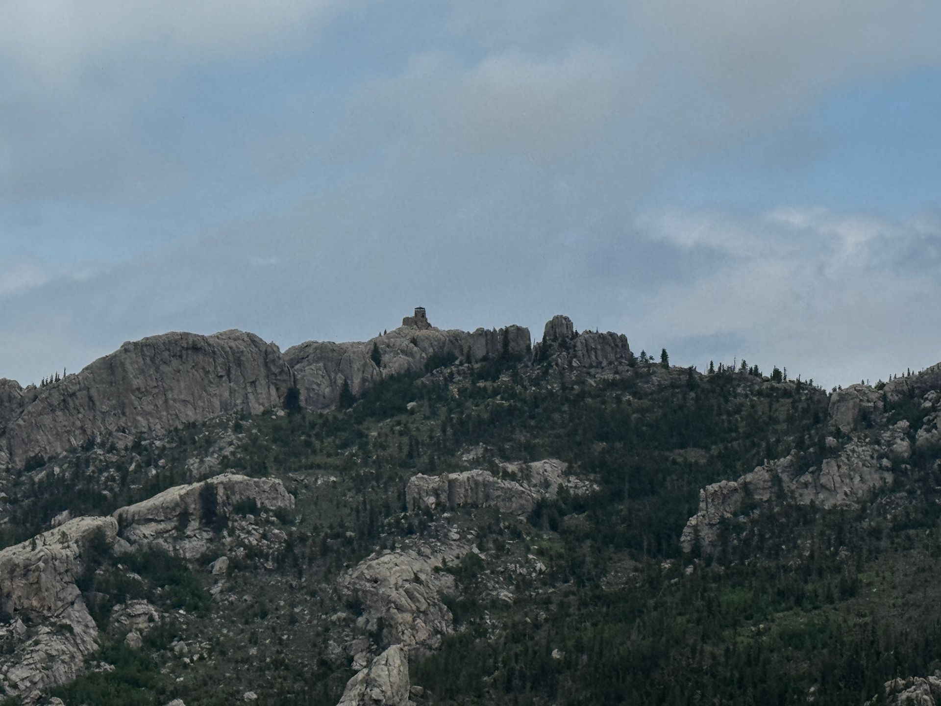Rocky mountaintop with a stone structure under a cloudy sky.