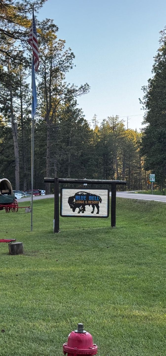 Sign with bison image in front of green field and trees with a red fire hydrant.