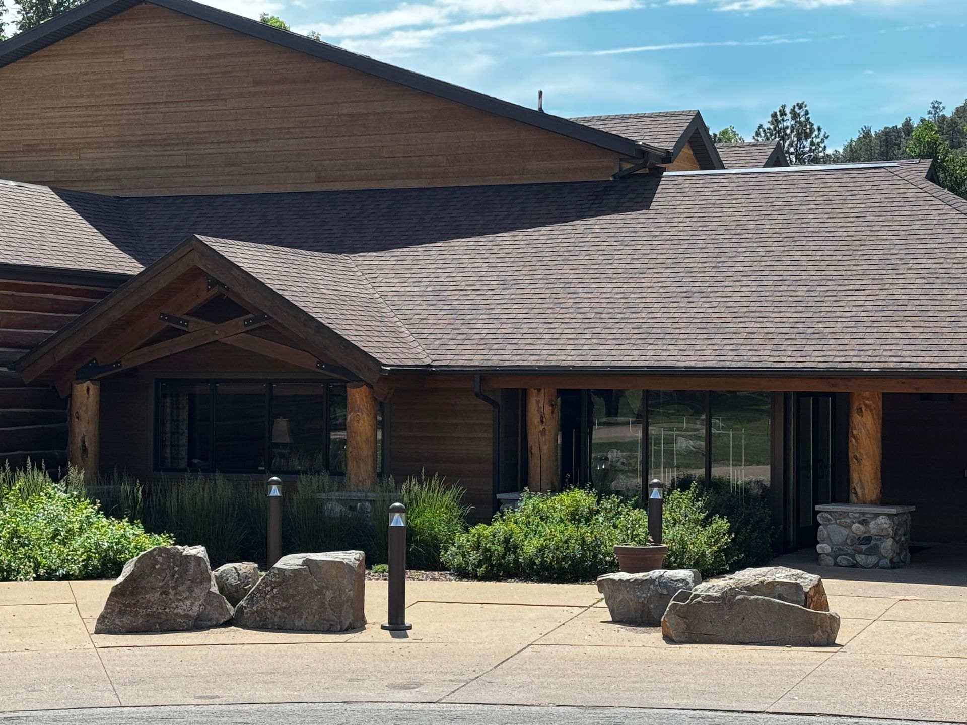 Lodge-style building with a wood exterior and stone accents, surrounded by greenery and rocks.