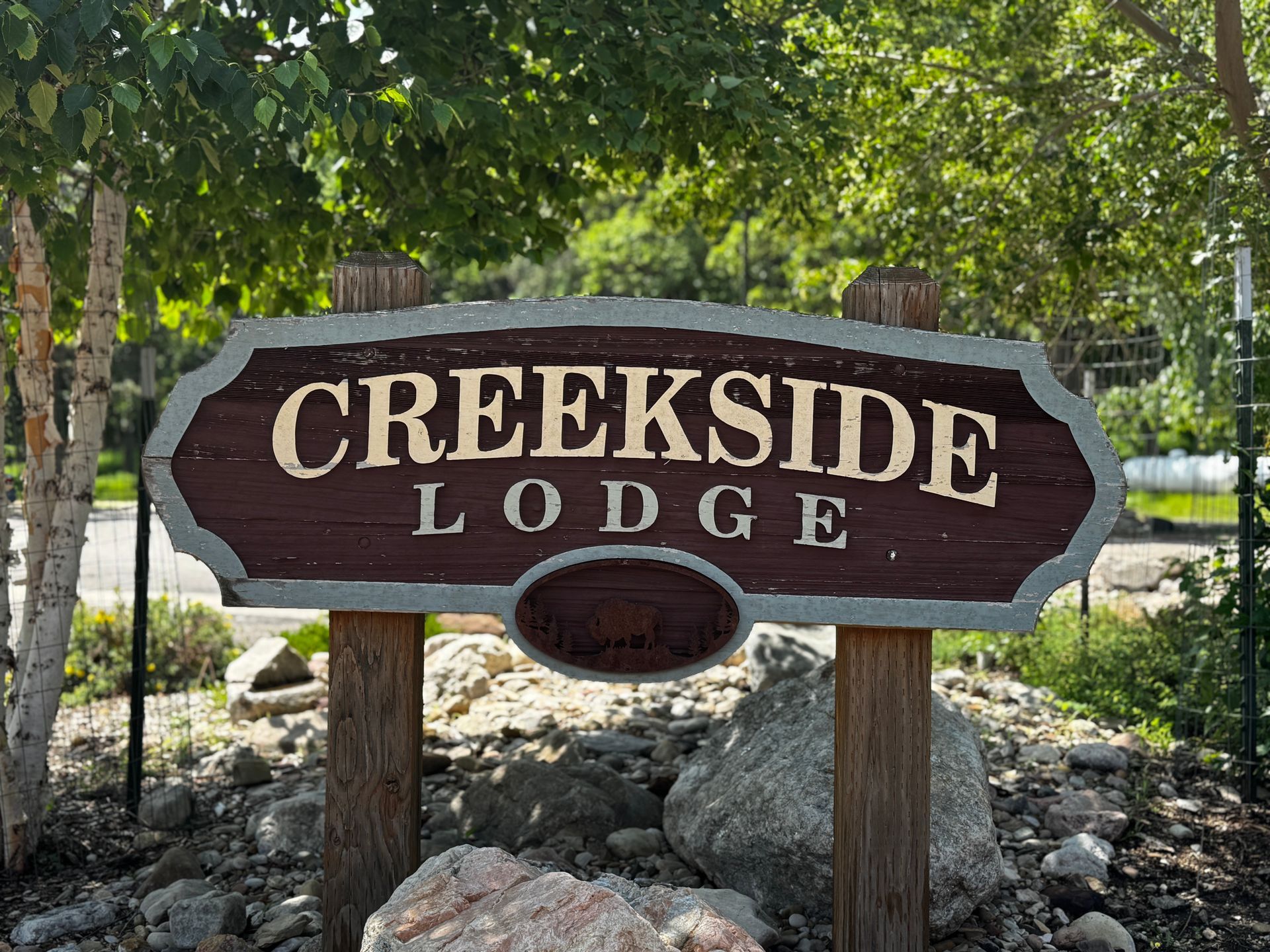 Sign for Creekside Lodge, brown with white lettering, set among rocks and greenery.