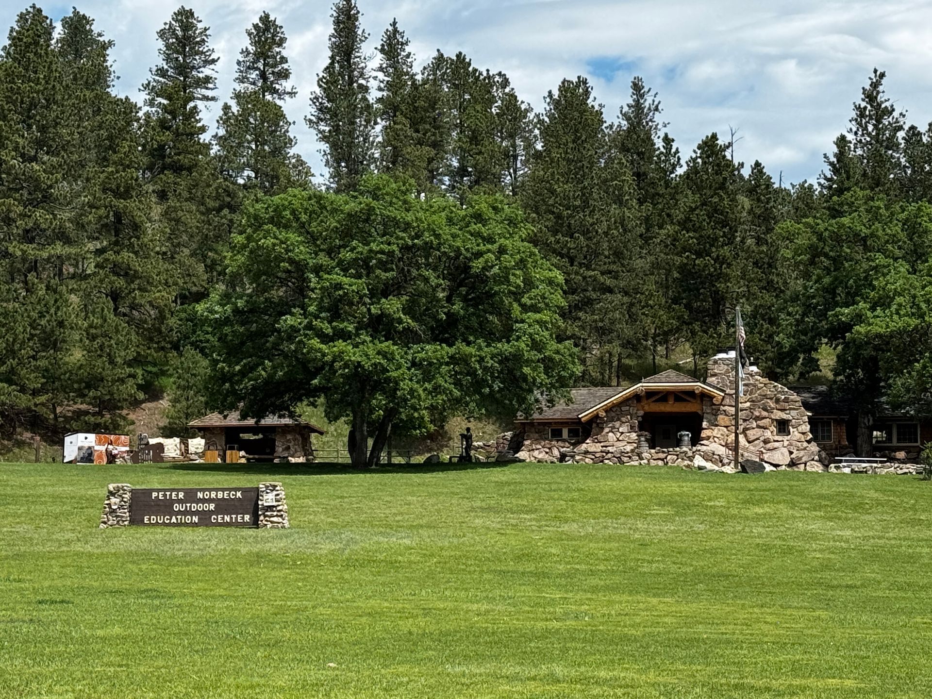 Lawn in front of a stone lodge, surrounded by trees. Sign in the foreground: 