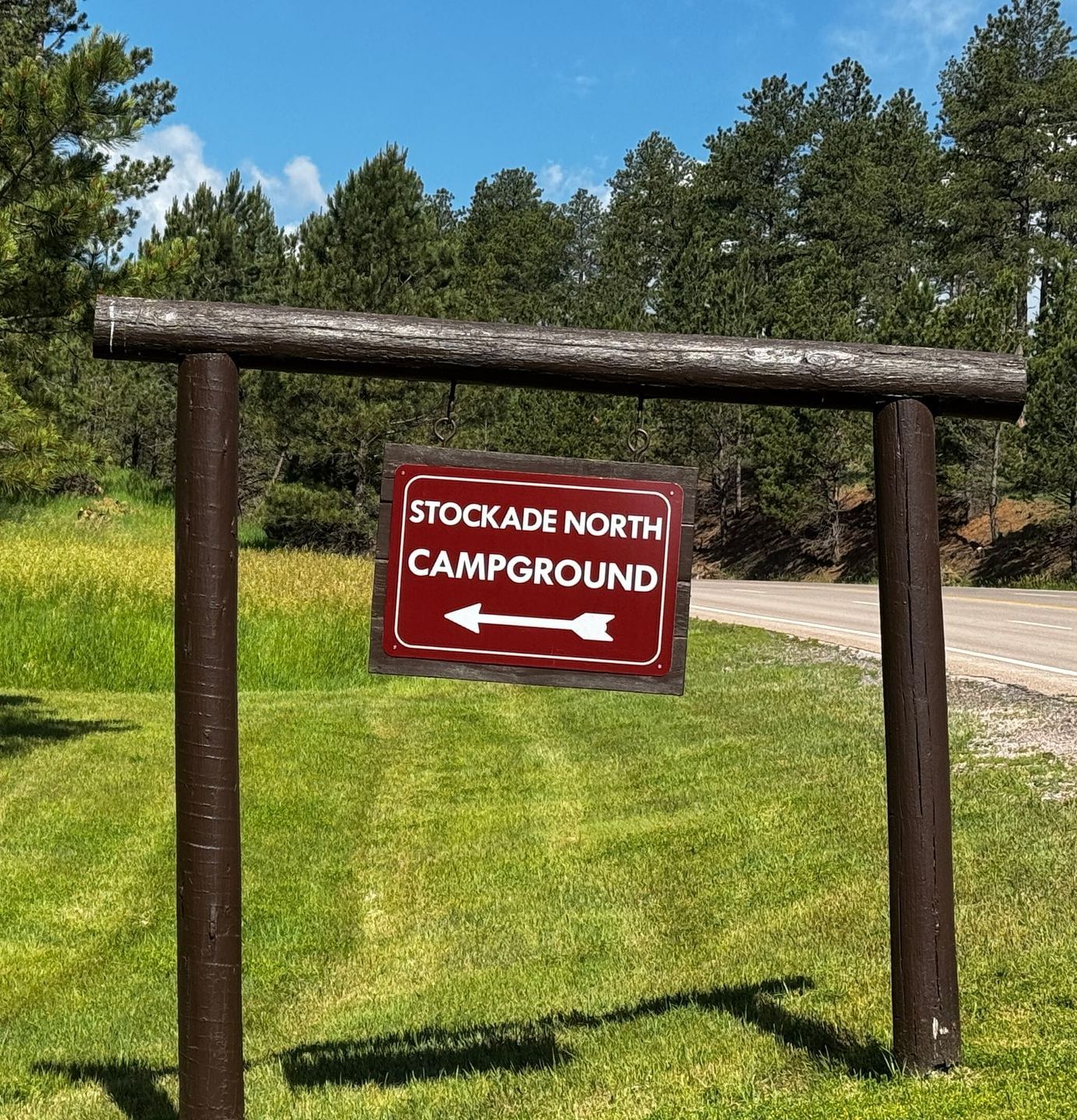 Sign for Stockade North Campground; brown posts, red sign with white arrow, green grass, trees, blue sky.