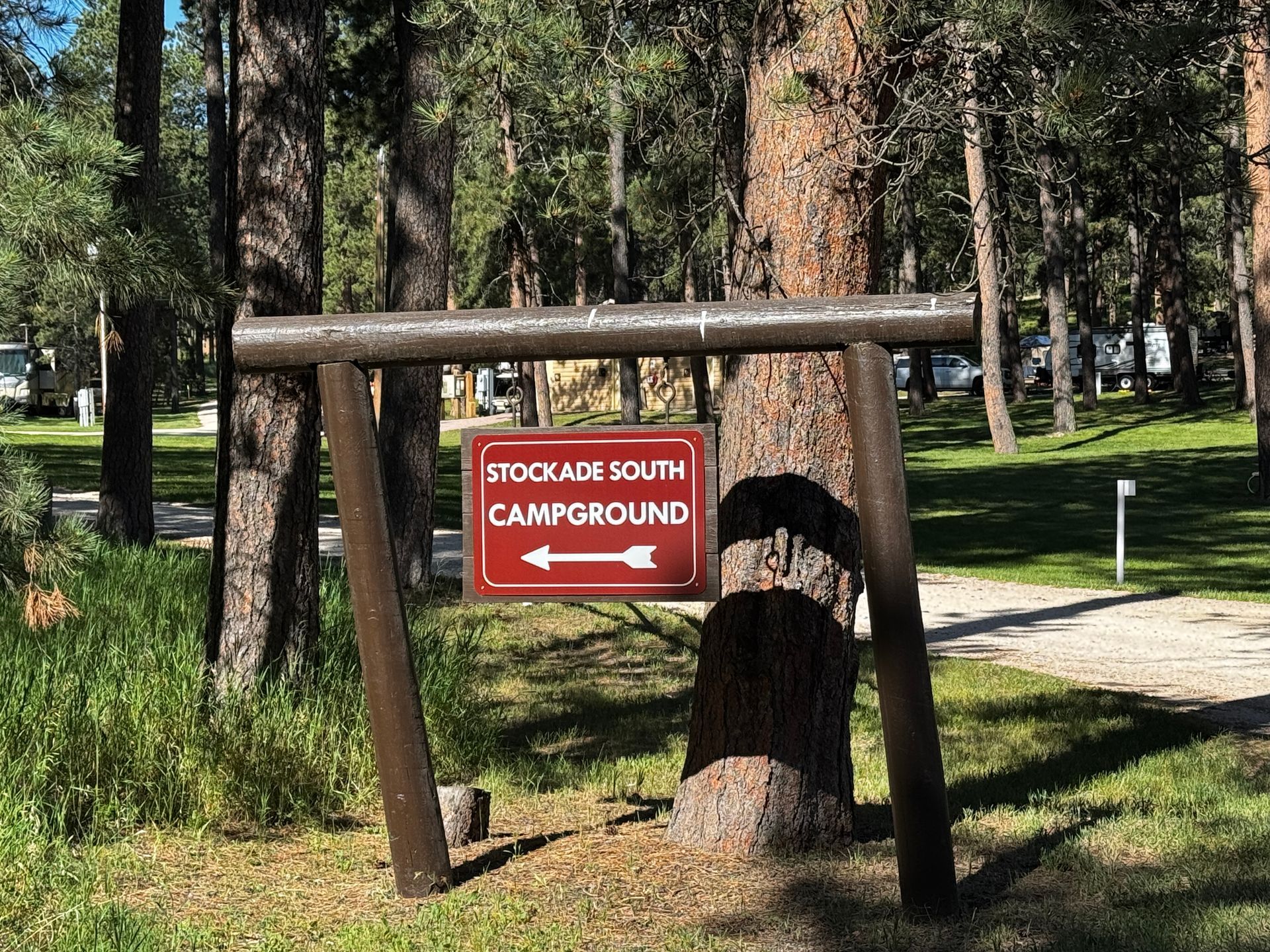 Sign for Stockade South Campground, brown wooden posts, red sign with white arrow. Forest setting.