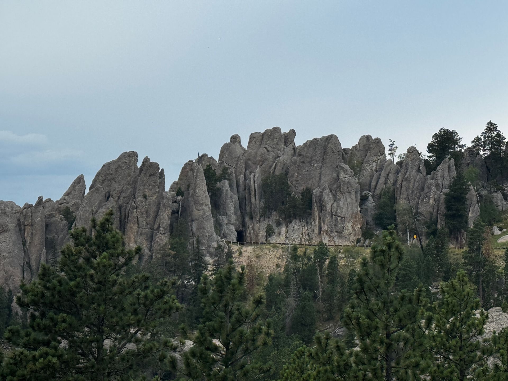 Jagged rock formations, with green trees in the foreground, under a cloudy sky.