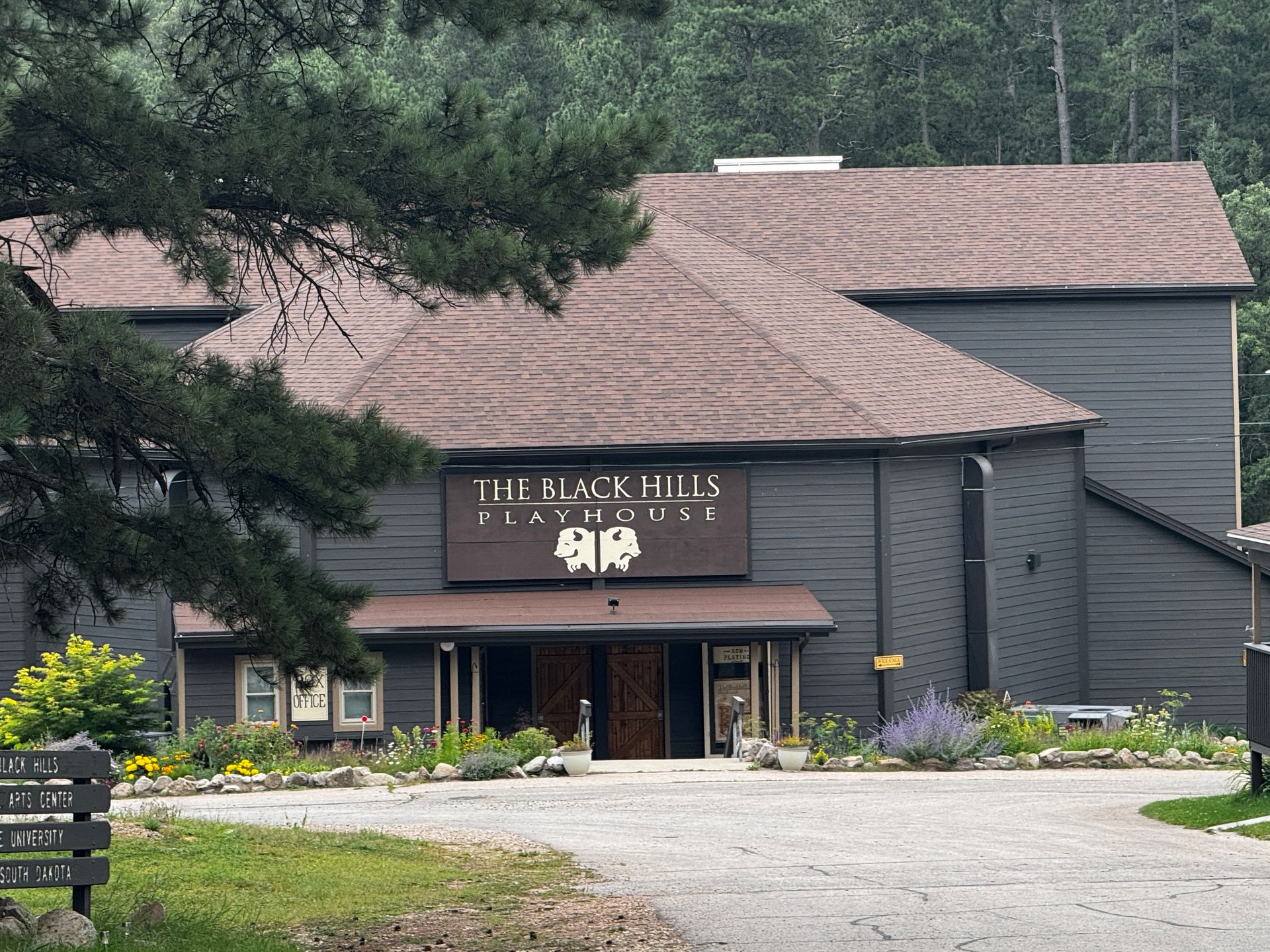 Black Hills Playhouse, a gray building with a brown roof, set amidst greenery.