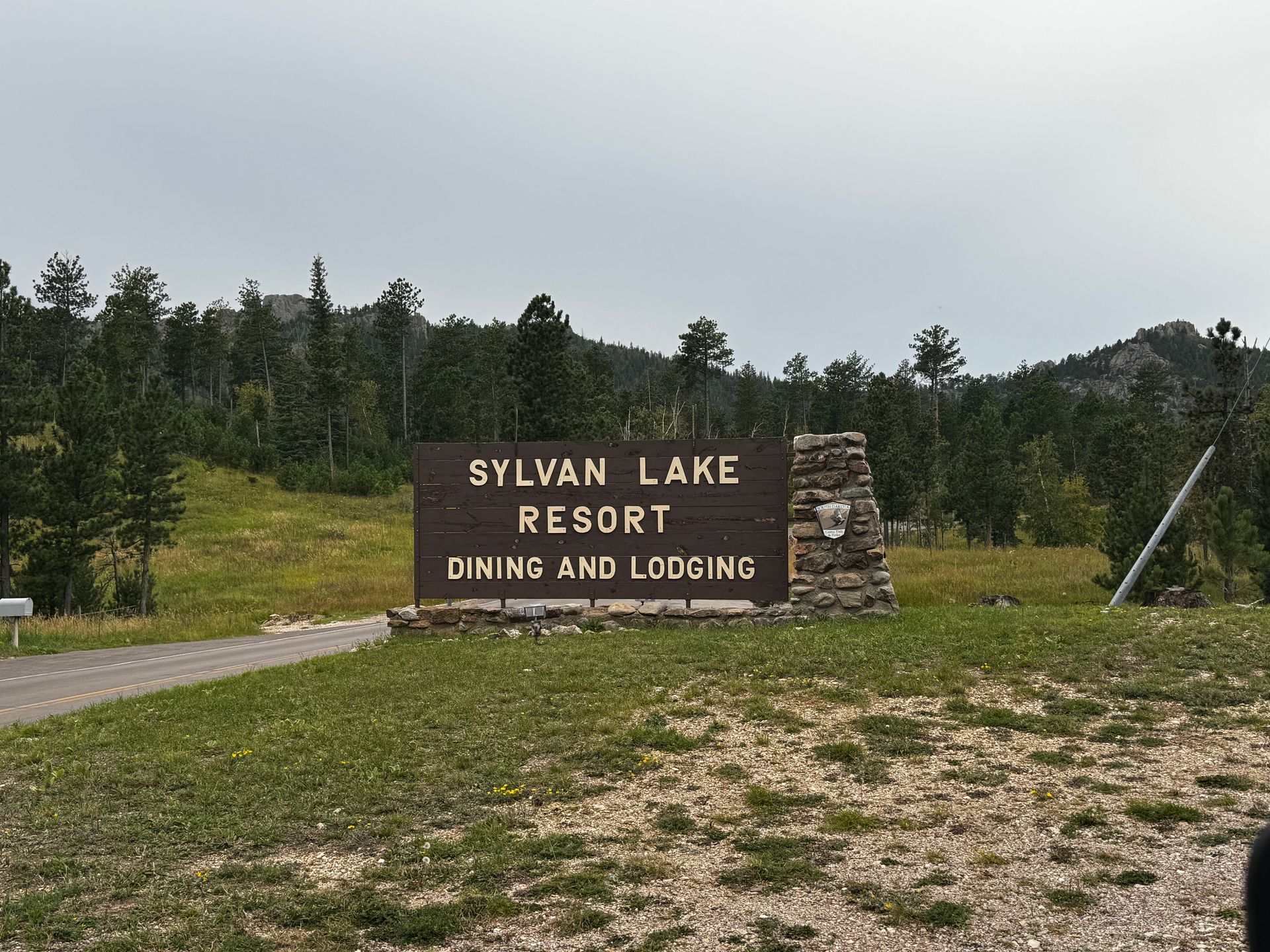 Sign for Sylvan Lake Resort, dining and lodging, in a natural setting, with trees and a cloudy sky.