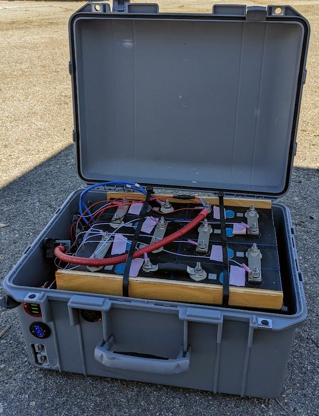 Open gray case with batteries, wires, and connectors, outdoors.