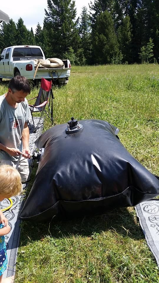Man filling a large black water bladder outside. A child and a pickup truck are also visible.