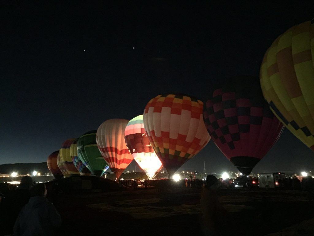 Hot air balloons lined up at night, glowing against a dark sky.