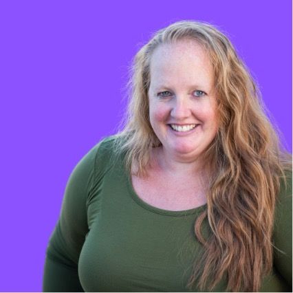 Woman with long wavy hair smiles, wearing a green long-sleeved shirt, purple background.