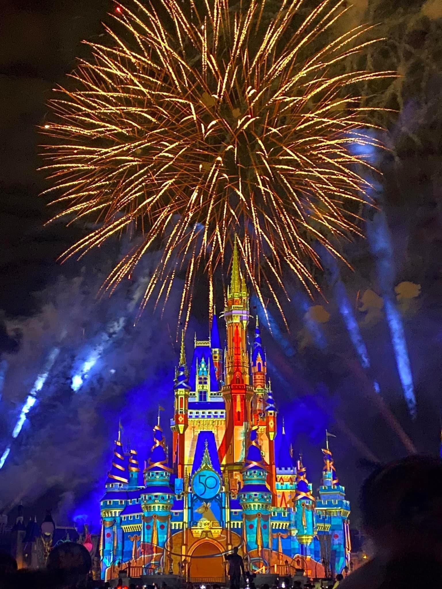 Fireworks explode above Cinderella's Castle at Disney World, illuminated by colorful projections.