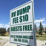 Sign for RV dump service: $10 fee, guests free. Pay at Picabo Anglers. Blue sky background.