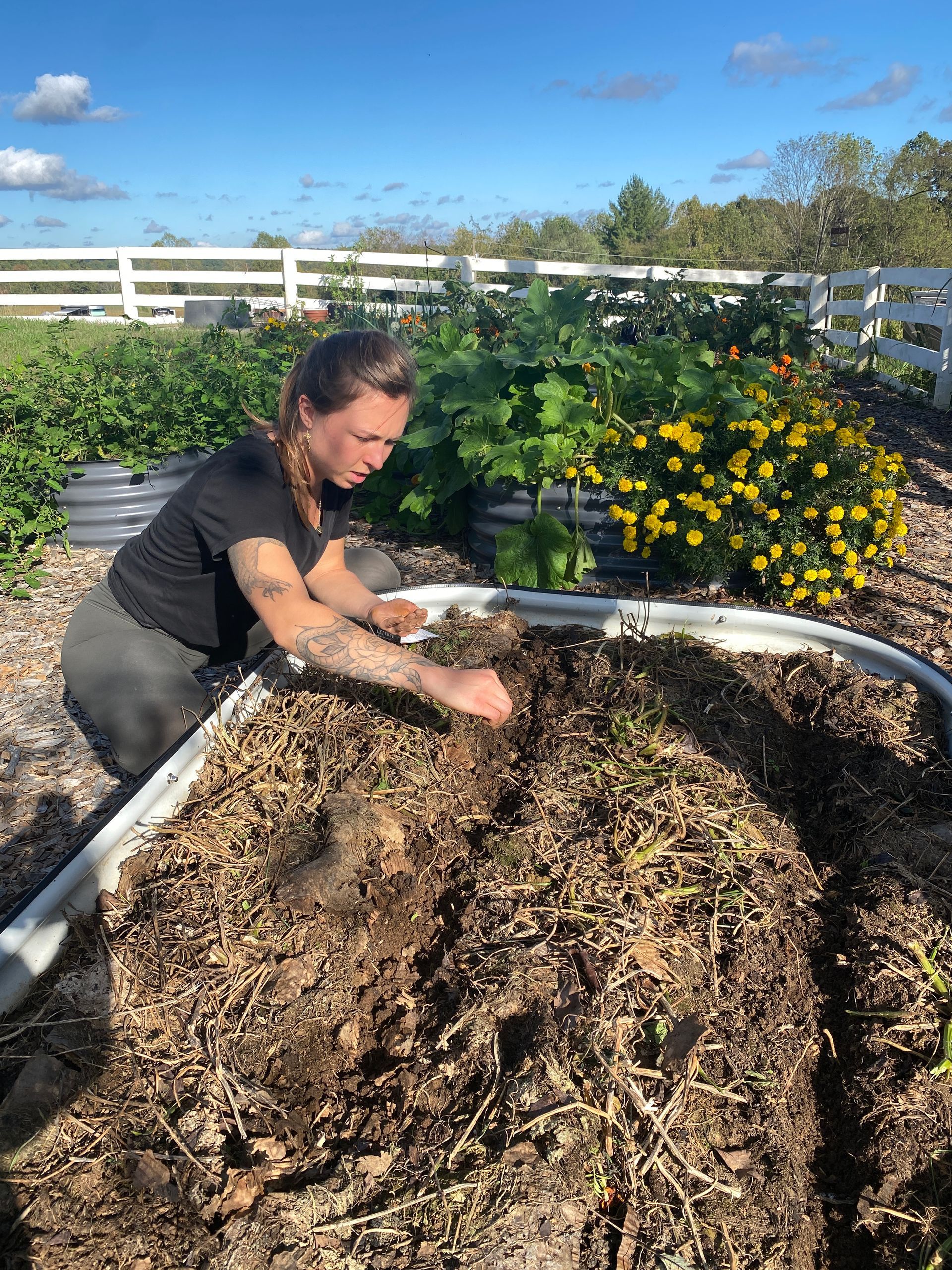 A woman is working in a garden with a fence in the background.