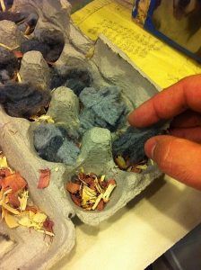 A person is holding a piece of blue wool in an egg carton.