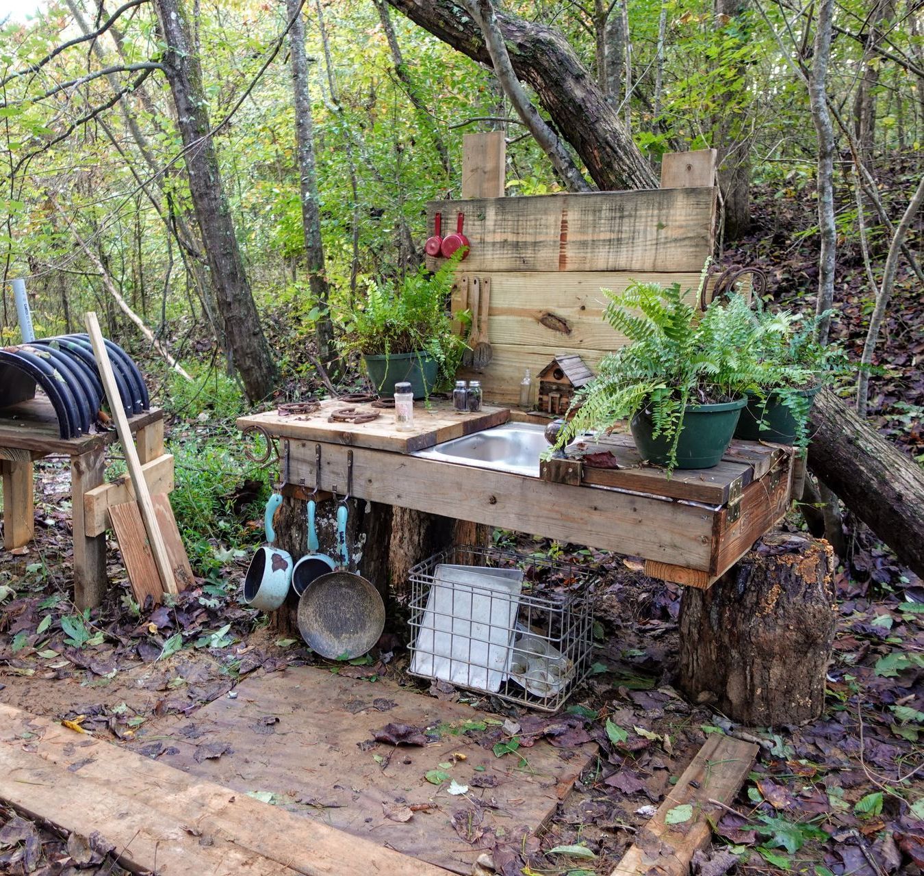 A wooden table with a sink and potted plants in the woods
