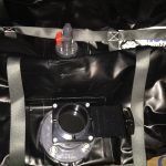 Black container with gray straps, a clear valve on top, and a black circular opening below.