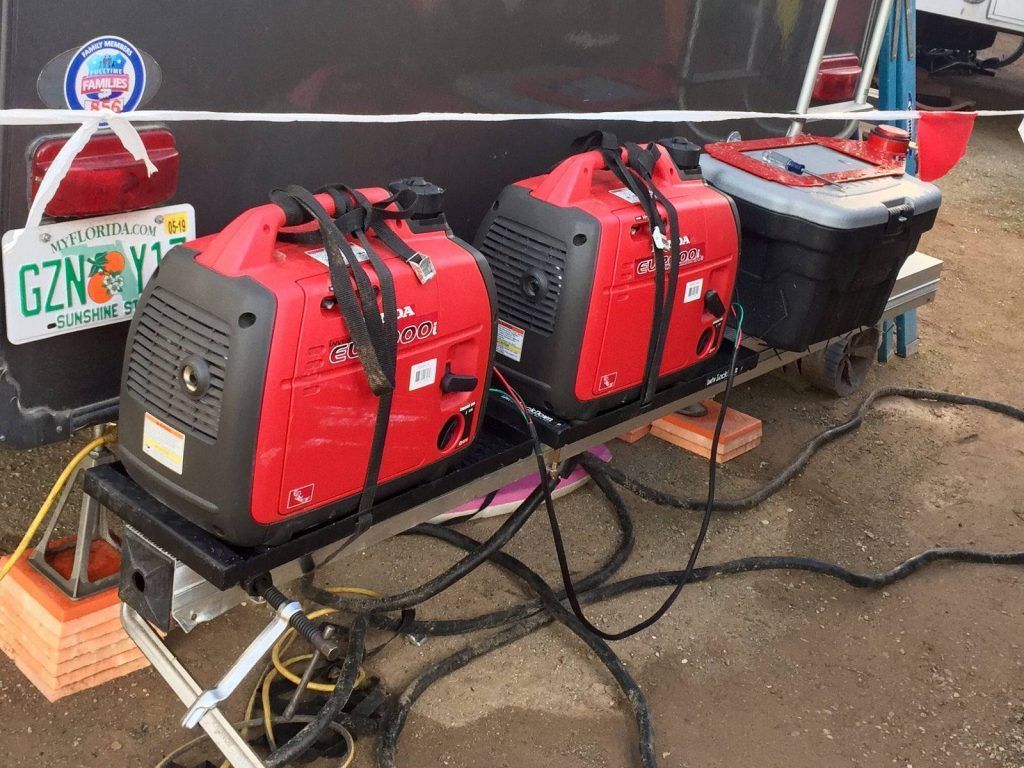 Three red generators are sitting on a cart next to a trailer.
