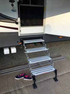 A pair of shoes are sitting on a rug next to a staircase leading to a rv.