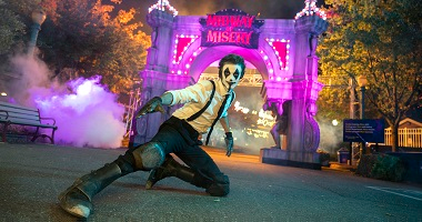 Clown in costume kneels, reaching towards camera, in front of 