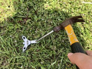 A person is holding a hammer and a wrench in the grass.