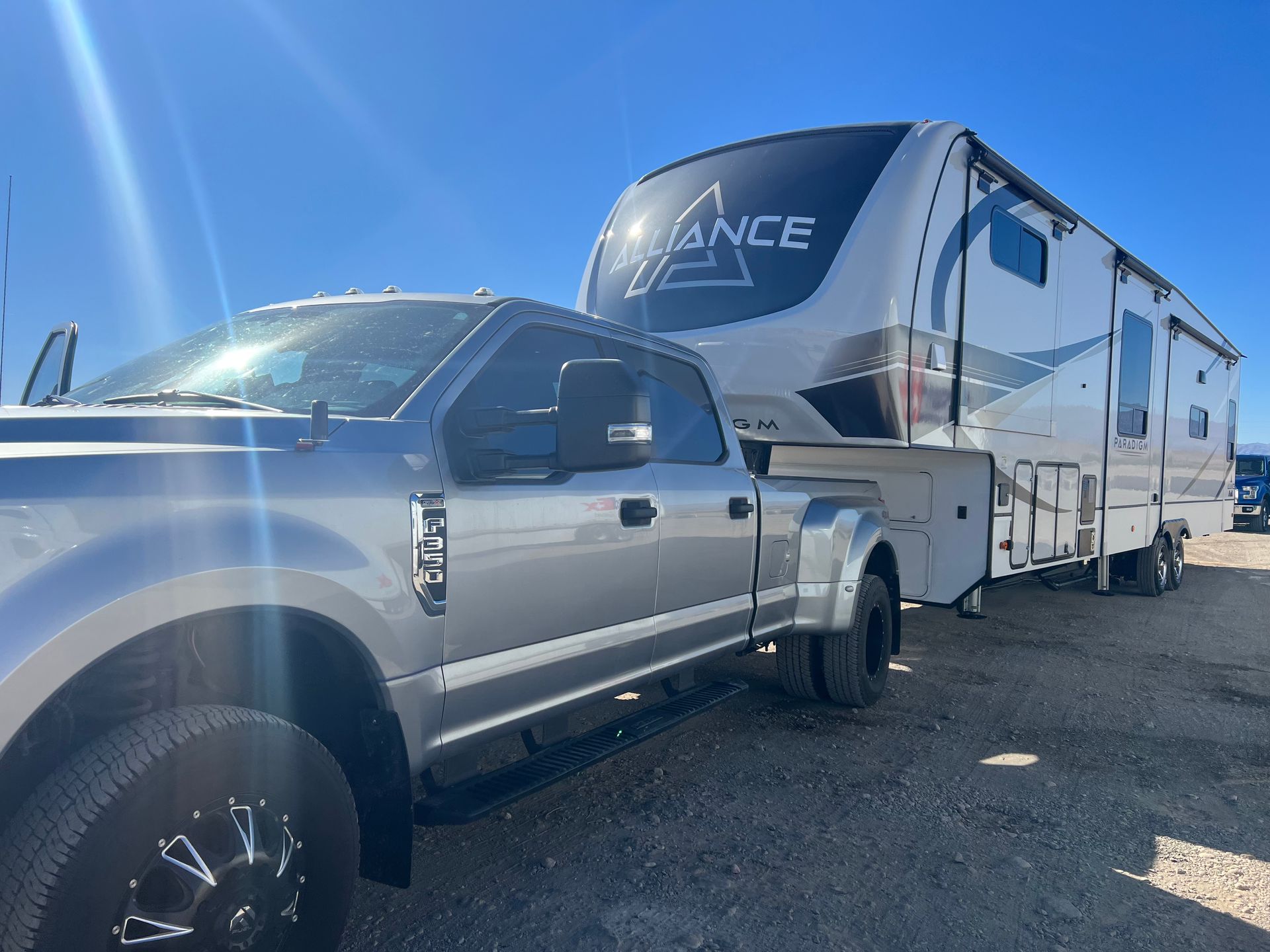 Silver truck towing a white Alliance fifth wheel RV on a sunny day.