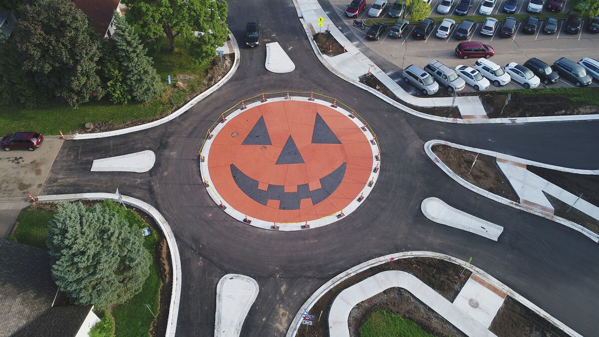 Aerial view of a pumpkin-painted roundabout; cars approaching and parked, with a Halloween theme.
