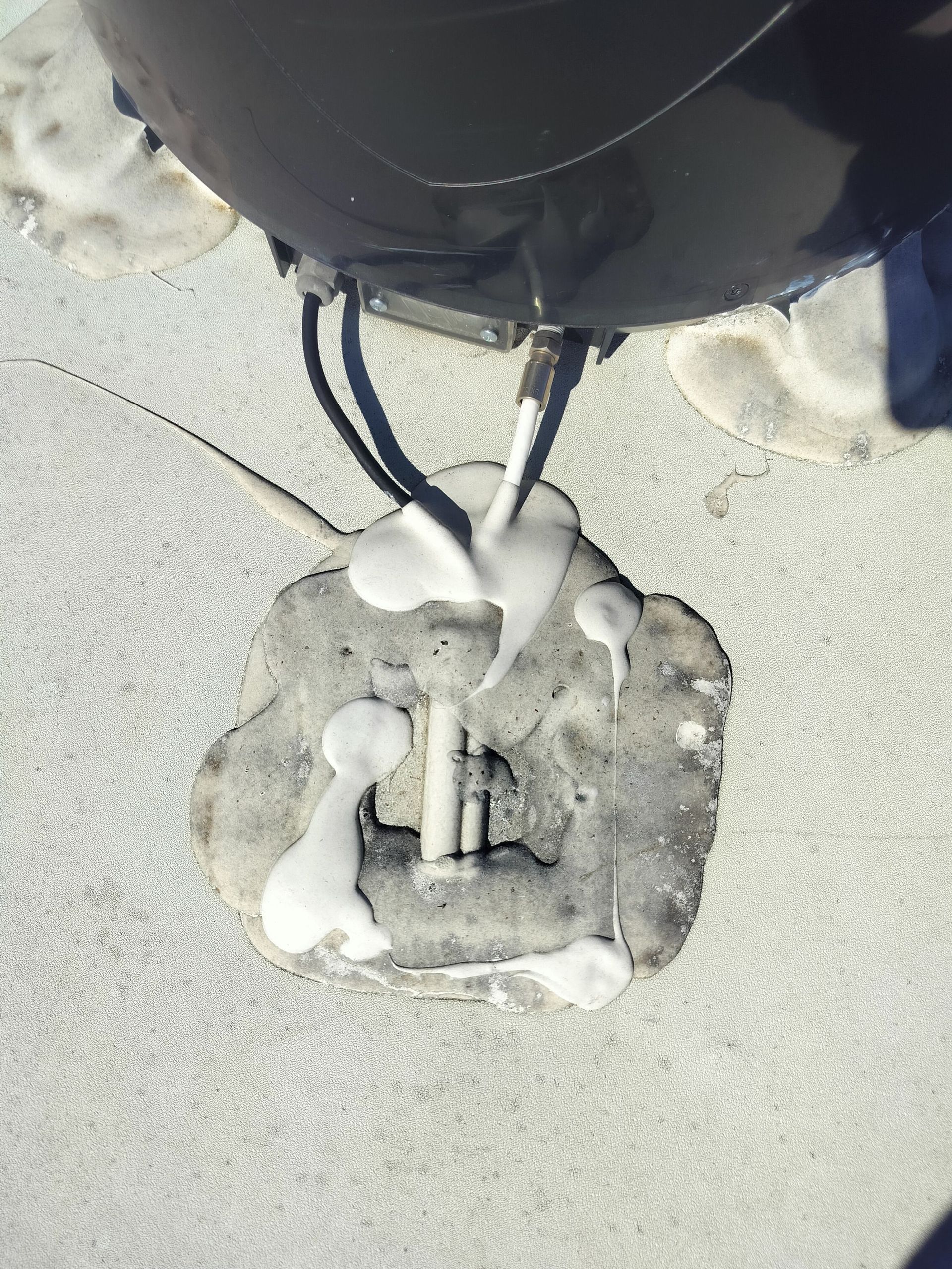 Layers of white sealant are applied around the base and cables where they enter the rv roof surface.