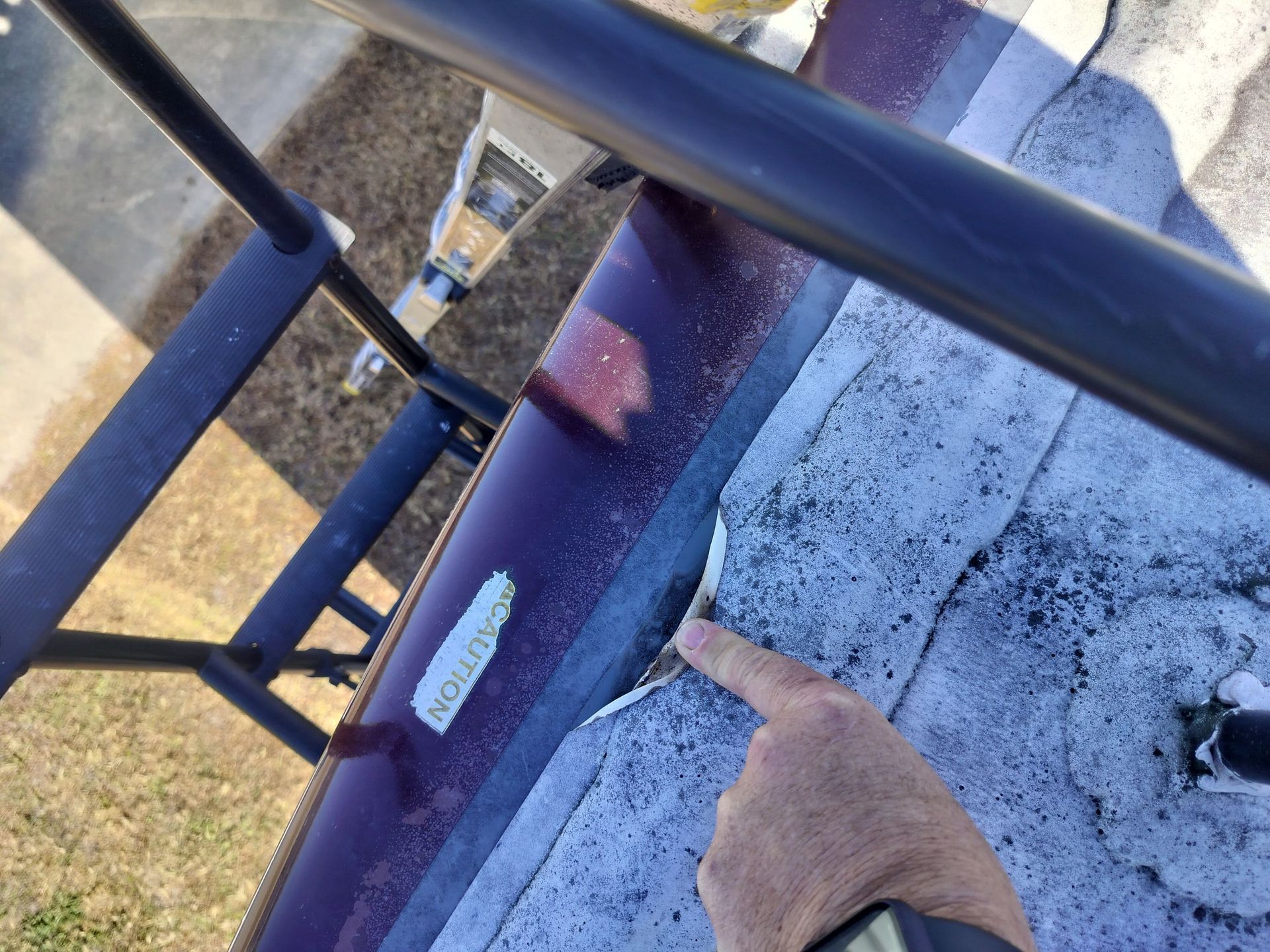 A finger points to a gap in the sealant along the edge of an RV roof, next to a black ladder.
