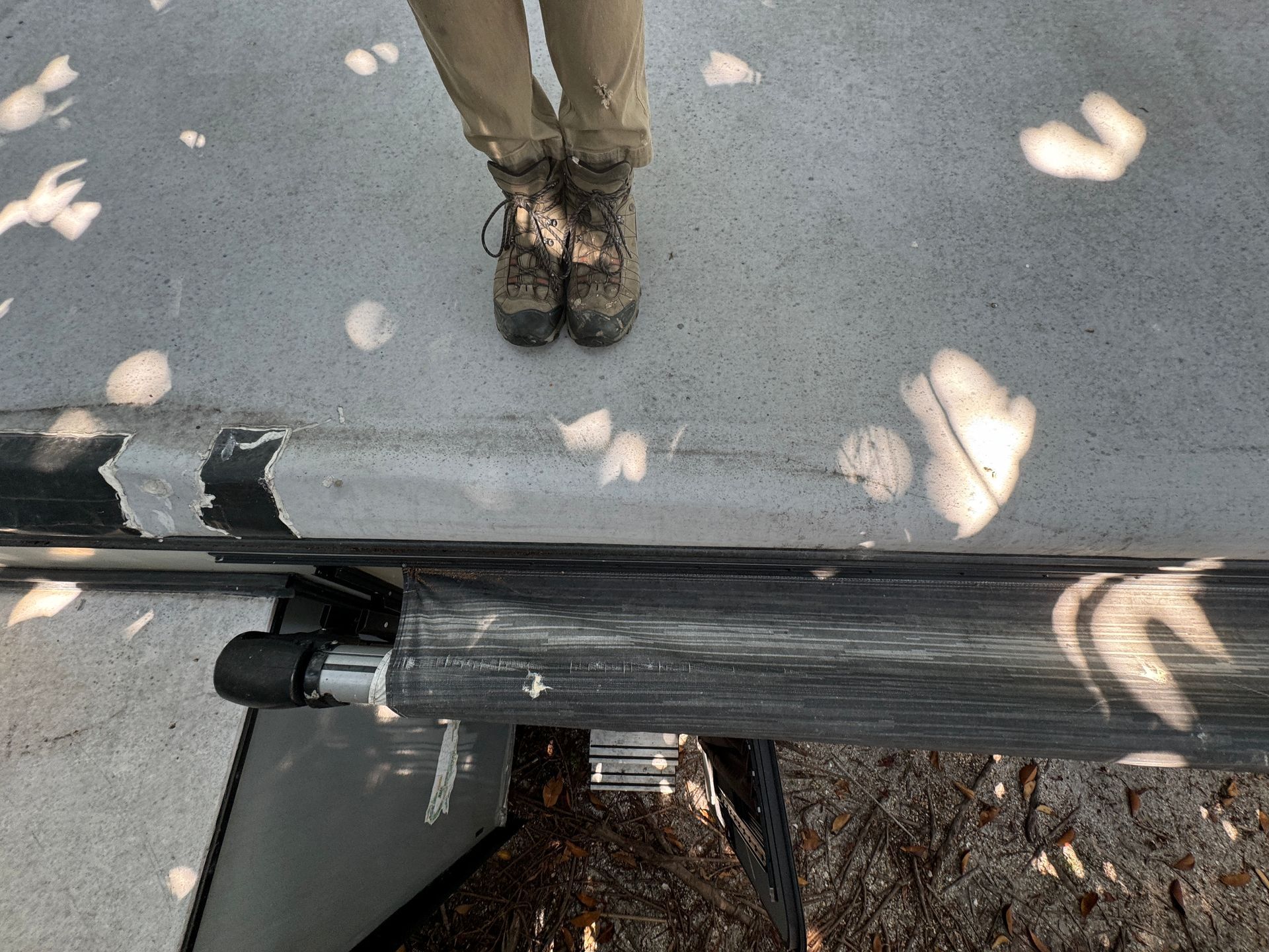 awning cover on an RV roof with a person’s boots on top of RV with scattered light and shadows