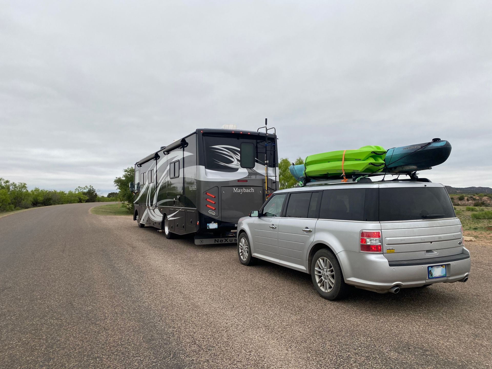 A silver suv is towing a rv with kayaks on top of it.