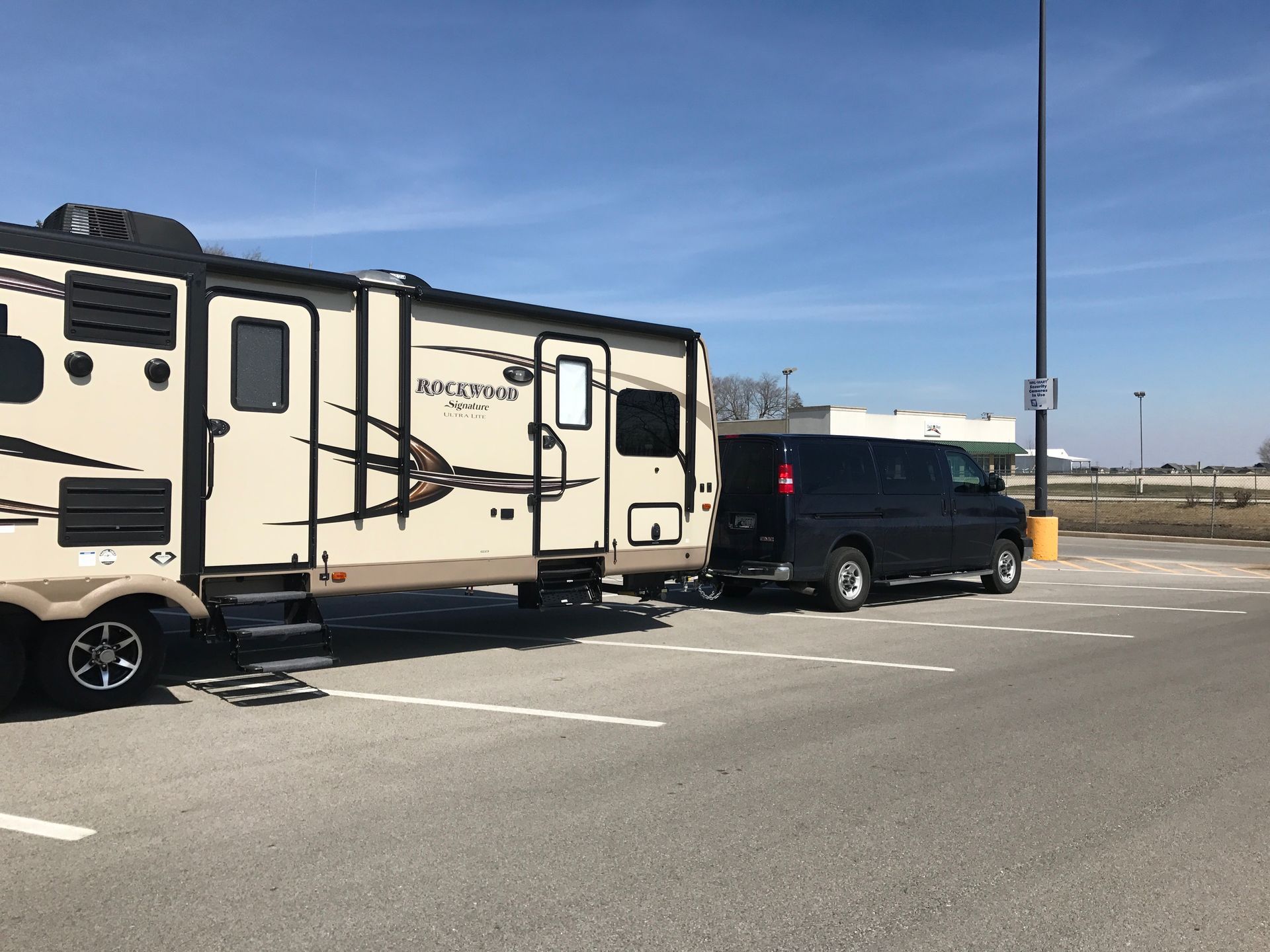 A rv is being towed by a van in a parking lot.