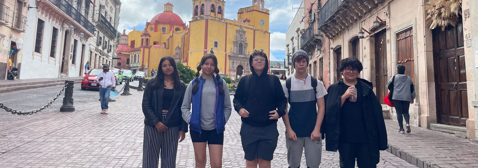 Five people stand on a cobblestone street in front of a large yellow building with a red dome.