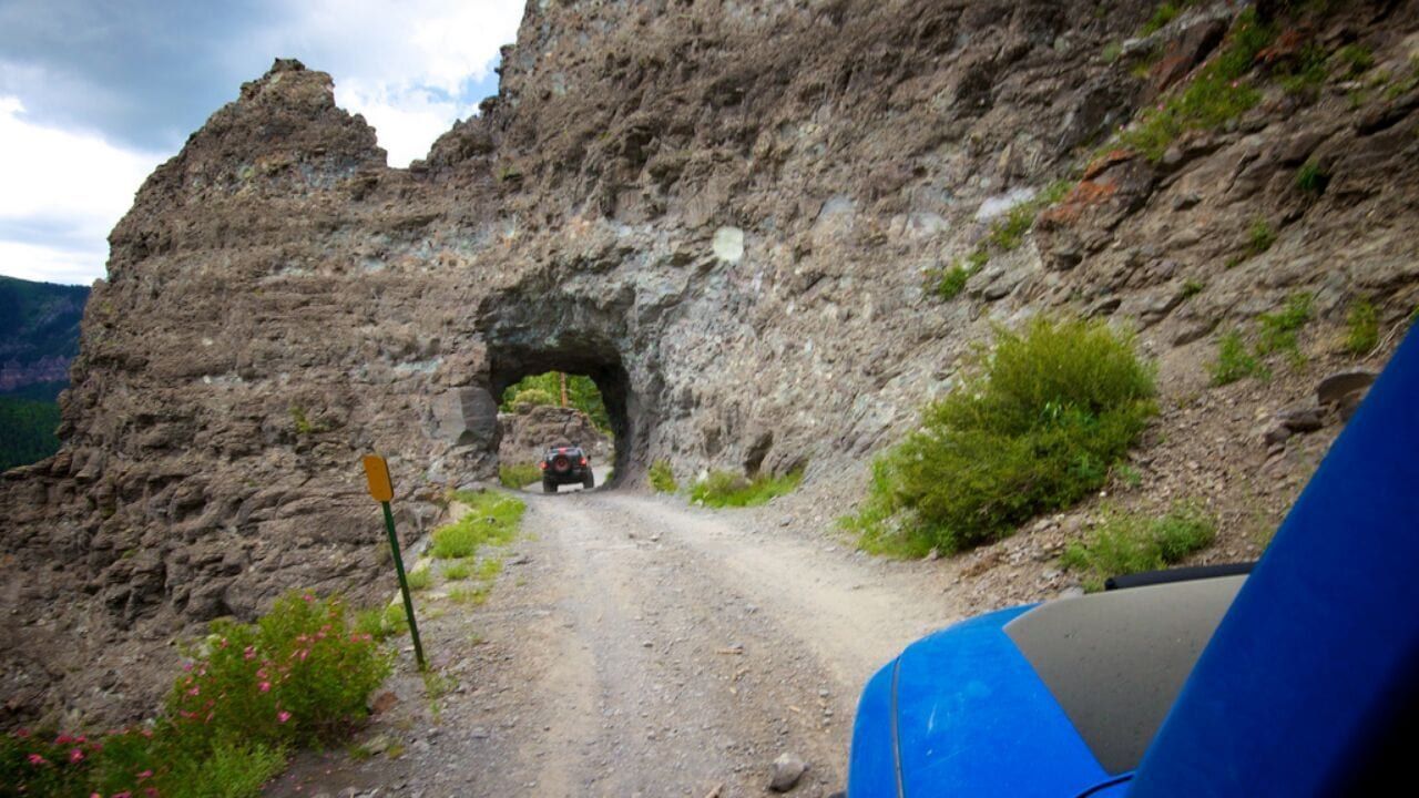 A car is driving through a tunnel on a dirt road.