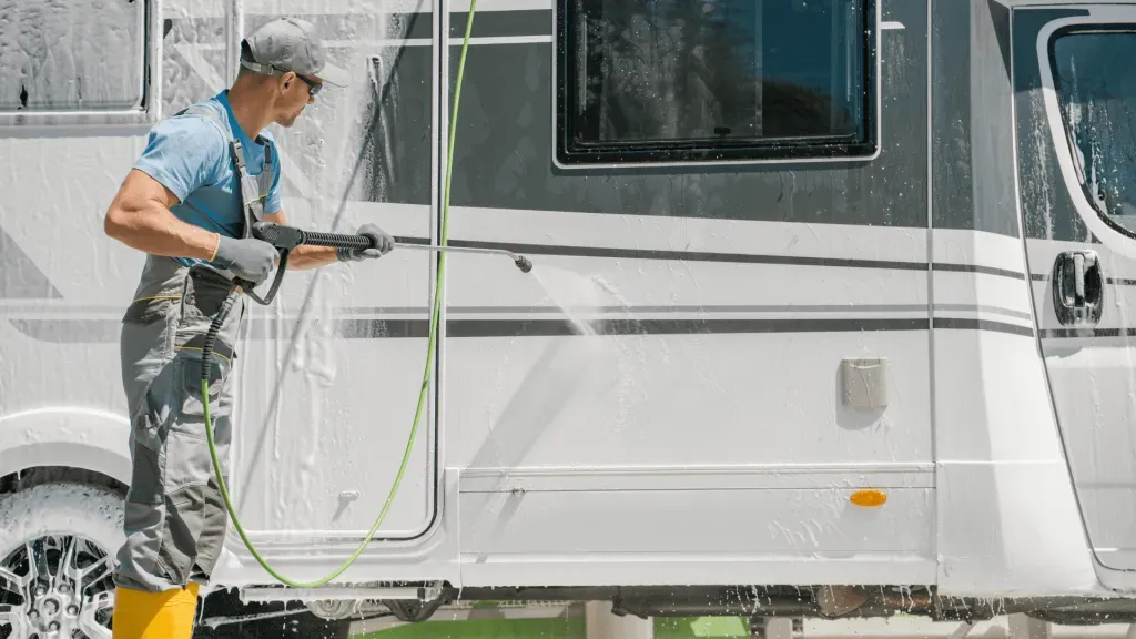 A man is washing a rv with a high pressure washer.