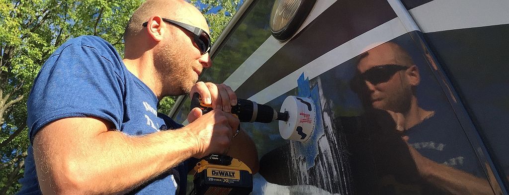 A man is using a drill to fix a window on a rv.