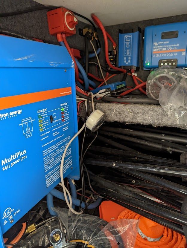 RV electrical components: blue inverter, chargers, wiring, and a disconnect switch.