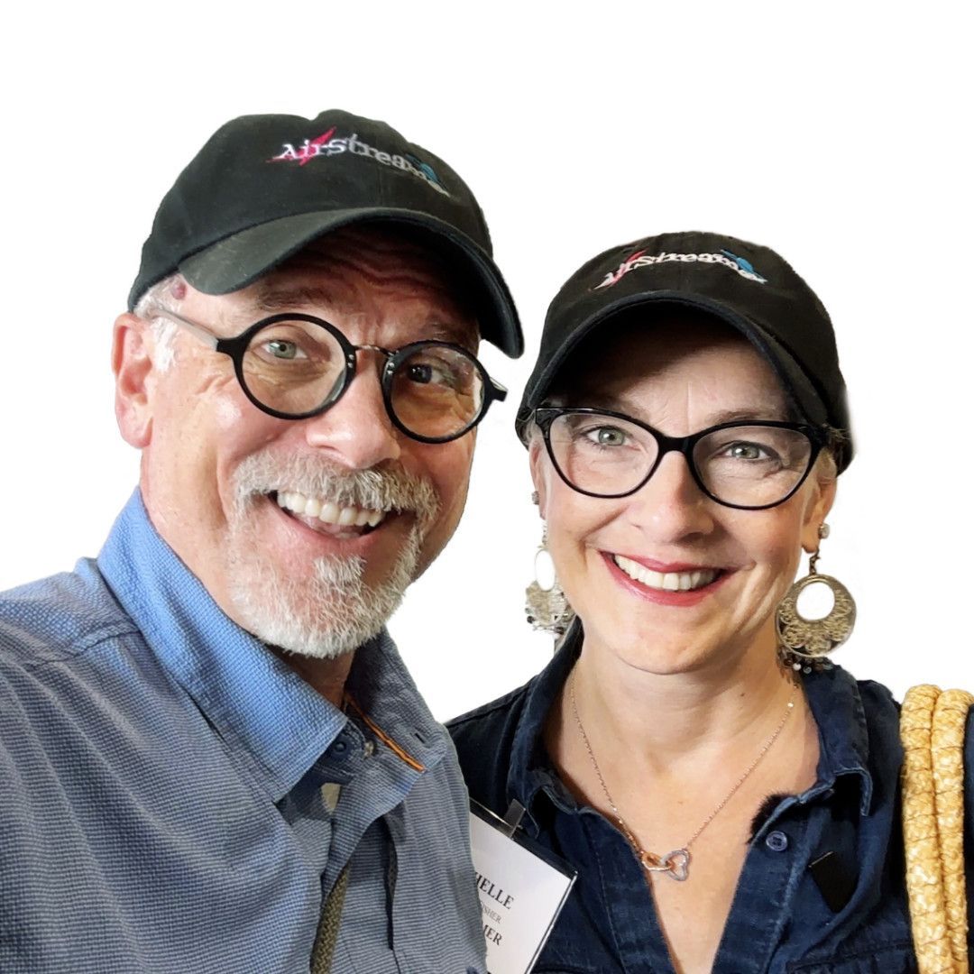 Man and woman smiling, wearing black caps and glasses.