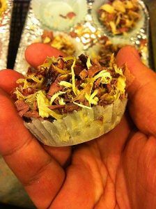 A person is holding a cupcake with meat and cheese in their hand.