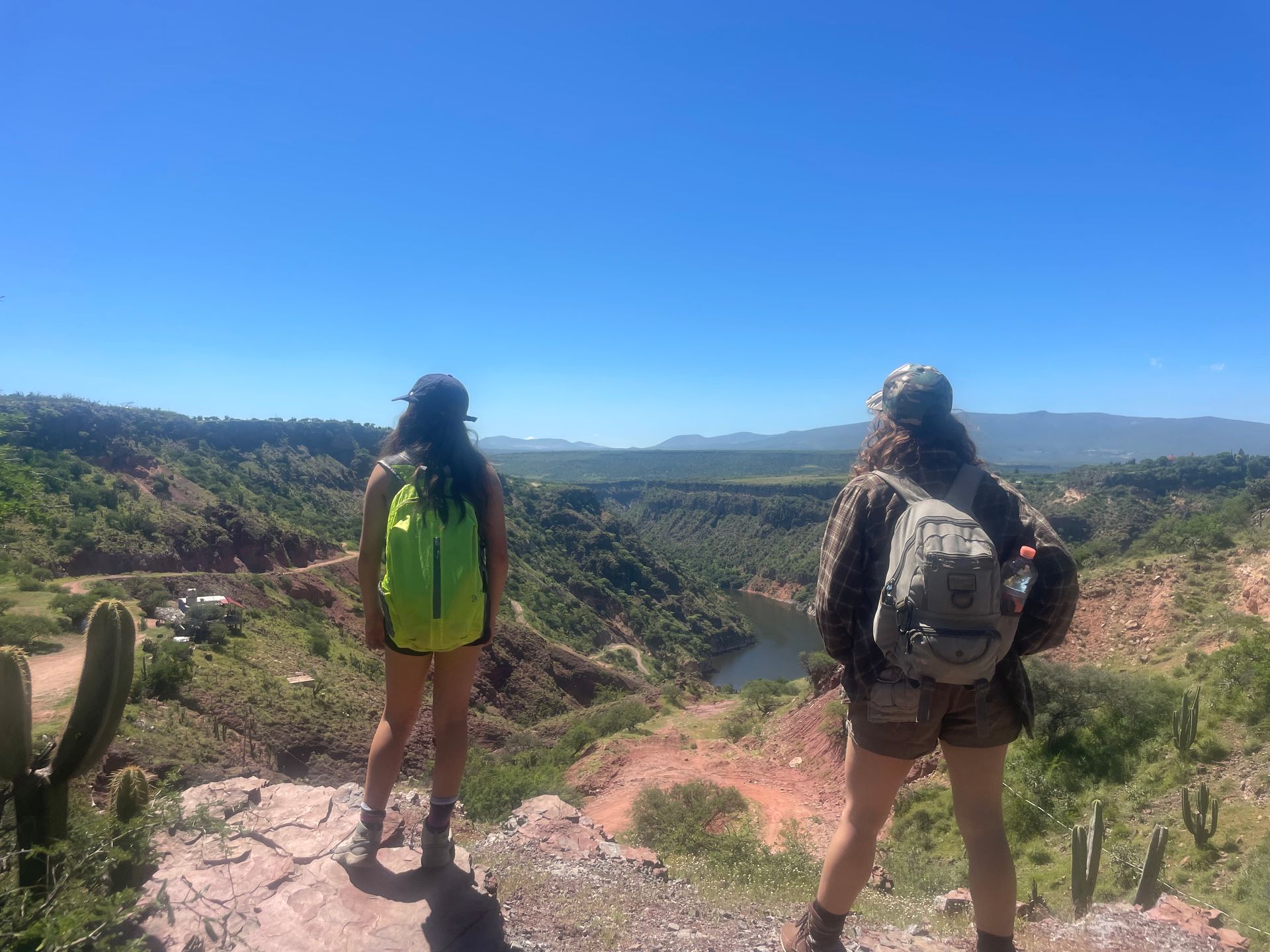 Two hikers overlooking a scenic canyon and river on a bright, sunny day.