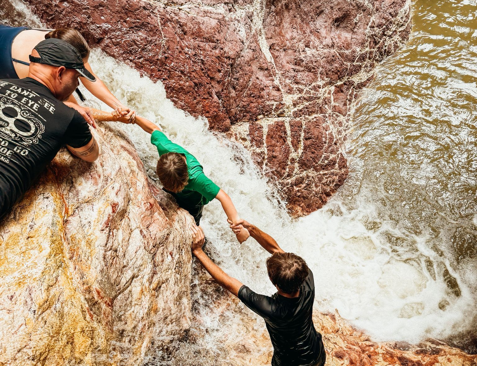People helping each other climb a wet, rocky waterfall.