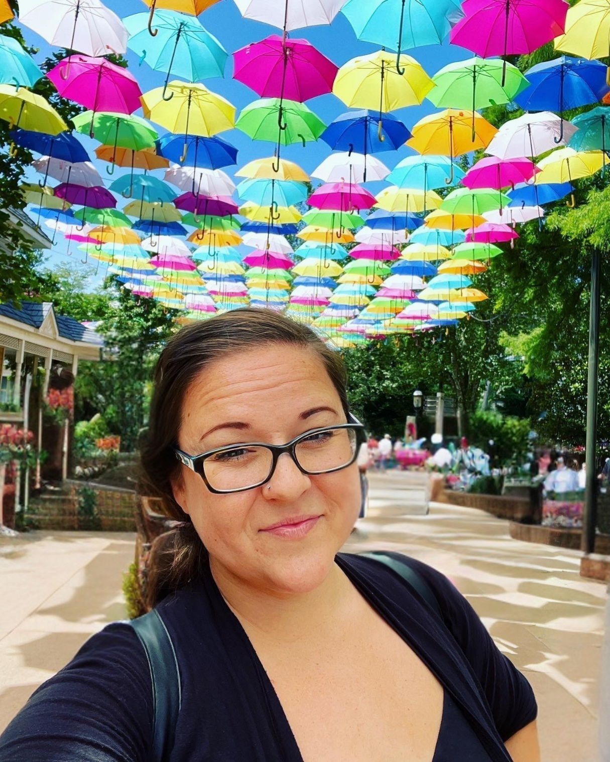 Woman with glasses smiles; dark hair at Dollywood under the umbrellas