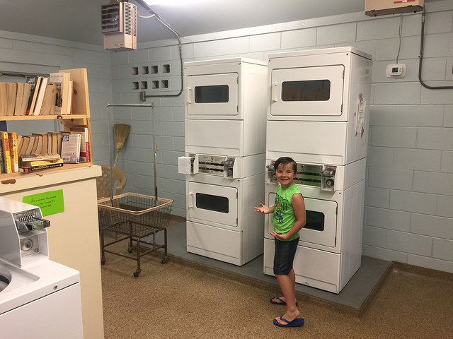 A little girl is standing in a laundromat next to a stack of washers and dryers.